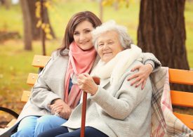 Senior,Woman,With,Cane,And,Young,Caregiver,Sitting,On,Bench